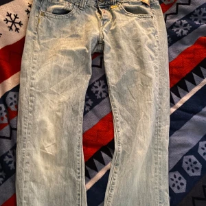 Ljusblå jeansbyxor - Säljer ett par ljusblå jeansbyxor med klassisk femficksdesign. Byxorna har en rak passform och är perfekta för en avslappnad stil. De har en knapp och dragkedja framtill.