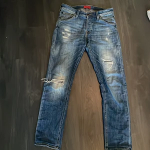 Blå jeans från Jack & Jones - Snygga blå jeans från Jack & Jones med slitna detaljer och en slim fit passform. Modellen heter Slim/Glenn och har storleken 30/32. Passar allt mellan 175 och 185, jag är 184 och de passar nästan inte men funkar ändå. Skick 10/10 i nyskick endast testade. Nypris: 949 kronor🔥