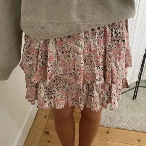 Mönstrad kjol från Zara - Säljer en söt, mönstrad kjol från Zara i rosa och vita med volanger. Kjolen har ett blommigt mönster och är perfekt för sommarn. Köpt för 250