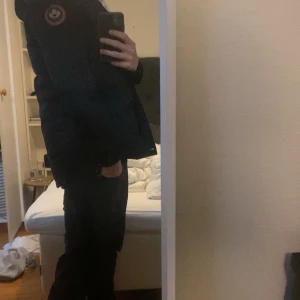 Svart parkajacka med pälsdetaljer - Säljer en svart parkajacka med pälsfodrad huva och flera praktiska fickor. Jackan har en dragkedja och knappar framtill samt en ikonisk logga på ärmen. Perfekt för kalla vinterdagar.han på bilden är 172. Priset är inte hugget i sten 🪨 tveka inte på o fråga nåt