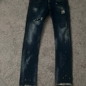 Mörkblå jeans från Zara - Snygga mörkblå jeans från Zara med slitna detaljer och färgstänk. De har en straight passform och klassisk femficksdesign. Perfekta för en avslappnad stil.