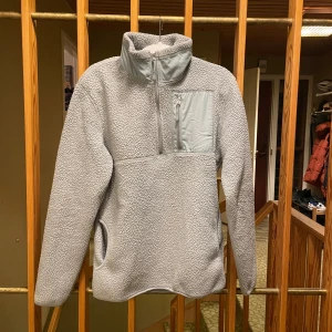 Grå fleece tröja från H&M - Mysig grå fleece tröja från H&M med dragkedja vid halsen och en praktisk bröstficka. Perfekt för kyliga dagar med sin mjuka och varma design. Tröjan har en normal passform och långa ärmar.