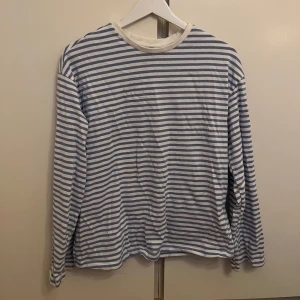 Randig långärmad tröja - OANVÄND  - Säljer en klassisk randig tröja i blått och vitt. Tröjan har långa ärmar och en rund halsringning, perfekt för en avslappnad stil. Helt oanvänd!