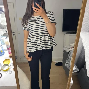 Randig topp med volangdetalj - Säljer en söt randig topp från Zara med korta ärmar och volangdetalj i nederkant. Toppen har ett klassiskt marinblått och vitt randigt mönster och är perfekt för en avslappnad stil.