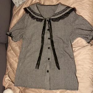 Kortärmad rutig  blus - Jag säljer en rutig söt blus som går att knyta åt vid kragen som en rosett. Är från Romwe