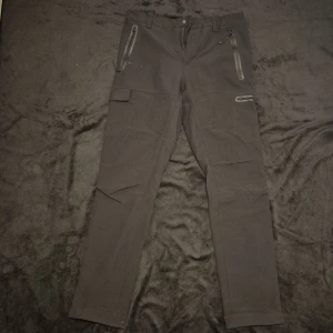 Svarta Everest cargopants med dragkedjor - Snygga svarta cargopants med praktiska dragkedjor på fickorna. Perfekta för en avslappnad stil med en touch av funktionalitet. Byxorna har en normal passform och är tillverkade i ett slitstarkt material.