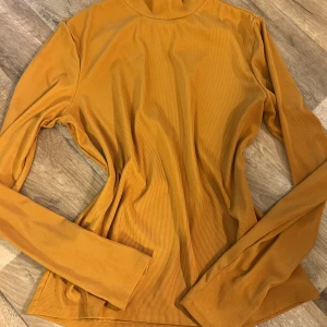 Orange ribbad polotröja - Säljer en snygg orange ribbad polotröja med långa ärmar. Perfekt för att hålla sig varm och stilren under kyligare dagar. Passar bra till både jeans och kjol.