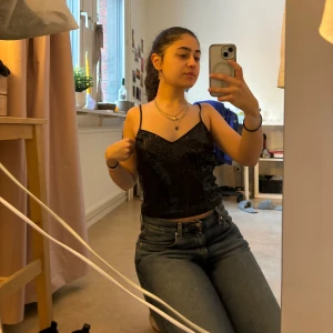 Svart paljettlinne från Morgan - Snyggt svart linne från Morgan med paljetter som ger en glittrig look. Linnet har smala axelband och en v-ringad design, perfekt för en festlig kväll.