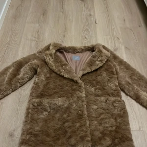 Brun pälsjacka från Lindex - Säljer en mysig brun pälsjacka från Lindex i storlek XS. Jackan har en mjuk och fluffig yta med långa ärmar och knäppning framtill. Perfekt för att hålla sig varm och stilren under kyliga dagar.