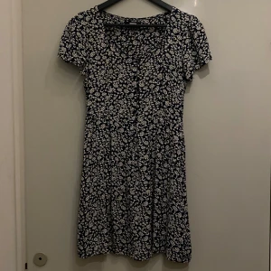 Blommig klänning från Bik Bok - Småblommig i stumt tyg. Knappar fram ner till midjan. Har fickor 