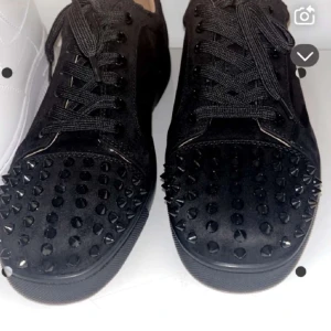 Svarta sneakers med nitar - Snygga svarta sneakers med nitar på ovansidan och en röd sula. Skorna har snörning och är tillverkade i mocka. Dem är oanvända.