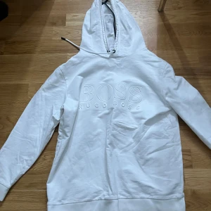 Vit hoodie från Hugo Boss - Säljer en stilren vit hoodie från Hugo Boss med broderad logga på bröstet. Tröjan har en klassisk design med huva och långa ärmar. Perfekt för en avslappnad look. Det är storlek S men passar även nån som har storlek M