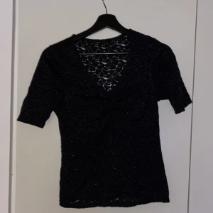 Svart spetsblus från Only - Snygg svart spetsblus från Only med korta ärmar och v-ringning. Perfekt för en stilren look. Blusen har ett vackert spetsmönster som ger en elegant touch.