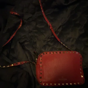 Röd axelväska från Valentino - Snygg röd axelväska från Valentino med nitar längs kanterna. Väskan har en justerbar axelrem och en dragkedja upptill. As snygg o passar till allt .pris kan diskuteras 