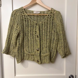 Grön stickad kofta från Cream - Säljer en snygg grön stickad kofta från Cream. Koftan har ett öppet stickmönster och knappar framtill. Den är perfekt för lager-på-lager och har trekvartsärmar som ger en avslappnad look. Passar bra till både jeans och kjol.