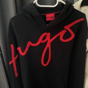 Hugo diraffe hoodie - Snygg svart hoodie från Hugo med ett stort rött logotyptryck över bröstet. Tröjan har en klassisk design med huva och en stor ficka framtill. Perfekt för en stilren och bekväm look. Sällsynt Hugo hoodie. Nypris 1699. Mitt pris 759