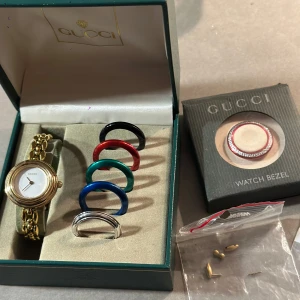 Guldfärgad klocka från Gucci med utbytbara ramar - Splitterny guldfärgad klocka från Gucci med 6 utbytbara ramar i olika färger. En lyxig grön förpackning och extra delar till bandet medföljer. Eftersom den är ny så fungerar den inte, så batteri fixar köparen själv. 2 små repor på displayen men inte synliga. Org pris: 7000kr