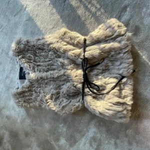 Beige pälsväst med knytband - Säljer en fluffig beige pälsväst från Vila. Västen har ett elegant knytband i midjan som ger en snygg siluett. Perfekt för att hålla sig varm och stilren under kyliga dagar.