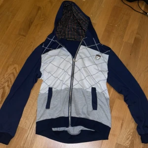 Blå och vit huvtröja från Weststreet Haku - Säljer en snygg huvtröja i blått och vitt från Weststreet Haku. Tröjan har ett rutigt mönster och dragkedja framtill. Den har en fodrad huva med rutigt mönster och två fickor. Perfekt för en avslappnad stil. Storlek XL men liten i storleken, passar bäst till M - L.