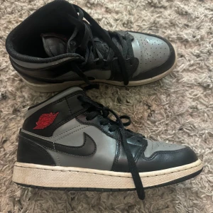 Nike Air Jordans i svart och grått - Säljer ett par Nike Air Jordans i svart och grått med röda detaljer. Skorna har en klassisk design med snörning och en bekväm sula. Perfekta för dig som älskar stil och komfort.