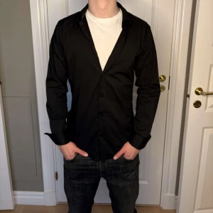 Svart skjorta med knappar - Snygg svart skjorta med knappar och långärmad design. Perfekt för en stilren look. Passar bra till jeans eller kostymbyxor.