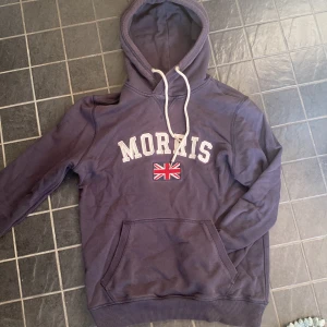 Mörkblå hoodie från Morris - Säljer en snygg mörkblå hoodie från Morris med vit text och en Union Jack-flagga på bröstet. 