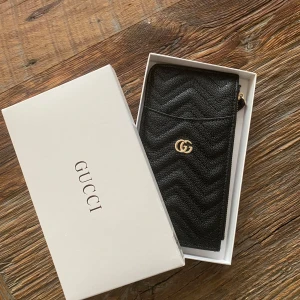 Clutch/korthållare - Svart clutch med guld-detaljer, ett fack med dragkedja, plats för flera kort. Längd 20 cm, höjd 11cm