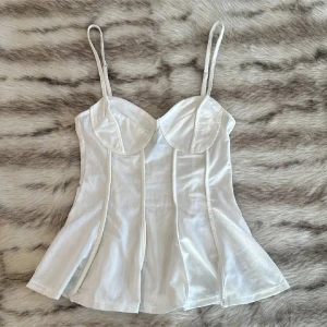 Vit korsett topp HM - Snygg vit korsett med tunna axelband och formade kupor. Den har en figurnära passform och lätt utsvängd nederdel. Perfekt för att skapa en stilren look 🎀