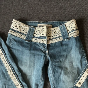 Lågmidjade bootcut med spetsdetaljer - Skitnygga blå bootcut jeans med spetsdetalj vid midjan och längs benen! De är lågmidjade och har en vintage stil. Storleken är 26 och de är uppsprättade nertill för att bli längre! Säljer då de tyvärr inte passar💕🎀