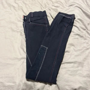 Mörkblå byxor med kontrastsömmar - Snygga mörkblå byxor från Whitaker med vita och röda kontrastsömmar. Tillverkade i en bekväm blandning av bomull, nylon och spandex för extra stretch. Perfekta för en avslappnad stil.