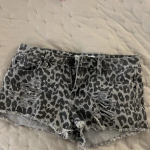 Grå leopardmönstrade jeansshorts från Maria Denim - Snygga grå jeansshorts med leopardmönster från Maria Denim. Shortsen har slitna detaljer och fransiga kanter för en trendig look. Perfekta för en avslappnad stil med en edgy touch.