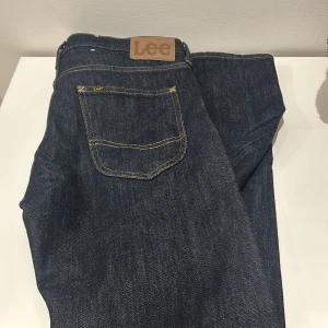 Slim fit jeans från Lee - Snygga mörkblå jeans från Lee med klassisk design och gul kontrastsöm. Perfekta för en stilren look. De har en slim passform. Om du har frågor så är det bara att fråga! Priset kan alltid diskuteras 
