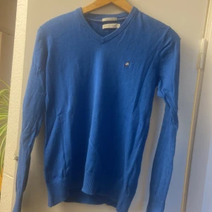 Blå kashmirtröja från Peak Performance - Säljer en snygg blå kashmirtröja från Peak Performance. Tröjan har en v-ringad design och långa ärmar, perfekt för kyligare dagar. Den är mjuk och bekväm med ribbade muddar vid ärmslut och nederkant. Perfekt för dig som vill ha stil och komfort i ett!