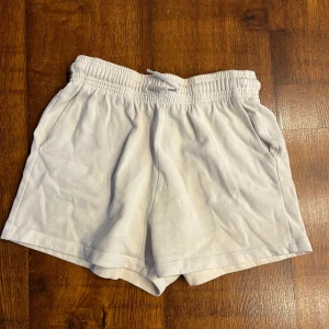 Vita mjukisshorts - Säljer ett par vita mjukisshorts med resårmidja och snörning. De har en avslappnad passform och är perfekta för varma dagar. Shortsen har två sidofickor och är tillverkade i ett mjukt material.