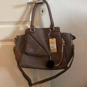 Brun axelväska från Vices - Snygg brun axelväska från Vices med guldfärgade detaljer och en dekorativ kedja.Perfekt för att ge din outfit en stilfull touch. Perfekt till skola då den får plats med dator böcker mm❤️ Har många väskor på min profil😁se sista bilden en liten defekt under som knappt syns❤️