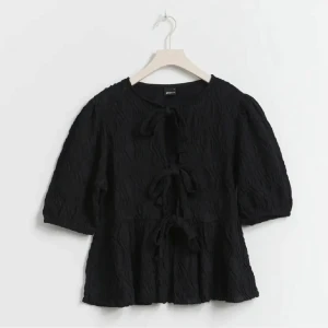 Svart blus med knyt - Snygg svart blus med trekvartsärm och knyt framtill. Blusen har en texturerad yta som ger en unik look. Perfekt för att lägga till en touch av stil till din garderob. 🧡