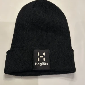 Svart mössa från Haglöfs - Snygg svart mössa från Haglöfs med en stilren design. Mössan har en uppvikt kant och en broderad logotyp framtill. Perfekt för kyliga dagar.
