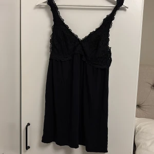 Svart nattlinne  - Snygg svart klänning med spetsdetaljer upptill och smala axelband. Perfekt för en elegant look. Klänningen har en mjuk och flödande passform som ger en bekväm känsla. Passar dig som är kortare än 165!