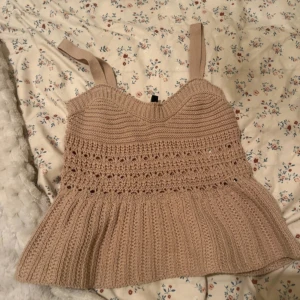 Beige stickad topp från Calliope - Säljer en söt beige stickad topp från Calliope. Toppen har breda axelband och ett vackert mönster med hålstickning. Perfekt för en avslappnad stil.