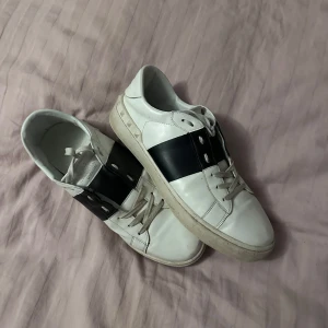 Vita sneakers med svart detalj - Snygga vita sneakers med en bred svart rem över sidan. Skorna har snörning och en klassisk design som passar till många stilar. Perfekta för en avslappnad look.