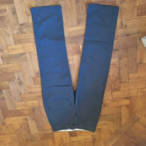 Grå byxor från Dickies - Snygga mörkblå byxor från Dickies, perfekta för en stilren look. Byxorna har en klassisk design med raka ben och två bakfickor. Tillverkade i ett slitstarkt material som ger en bekväm passform.