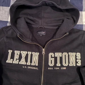 Marinblå hoodie från Lexington - Säljer en marinblå hoodie från Lexington med dragkedja och tryck framtill. Hoodien är i storlek (S) och är lite för liten för mig som är 183cm. 
