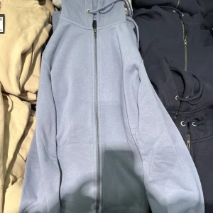 Ljusblå hoodie med dragkedja - Säljer en ljusblå hoodie med dragkedja och justerbar huva. Perfekt för en avslappnad stil. Den har långa ärmar och en bekväm passform.