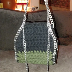 Virkad väska med kedjedetaljer - Unik virkad väska i svart och grön med silverfärgade kedjedetaljer. Perfekt för att ge din outfit en cool touch. Väskan har en rymlig design.