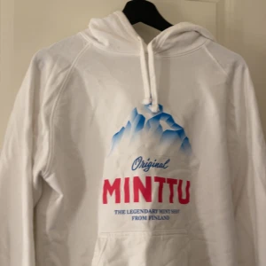 Vit hoodie med Minttu-tryck - Säljer en vit hoodie med  Minttu-tryck på framsidan. Hoodien har en klassisk design med dragsko i huvan och en stor ficka framtill. Perfekt till afterski, helt ny endast testad. Skriv om du undrar nått ❤️Kan gå ner lite i pris vid snabb affär 