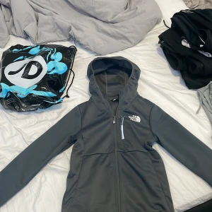 Grå jacka från The North Face - Säljer en grå jacka från The North Face med huva och dragkedja. Jackan har en stilren design med The North Face-logga på bröstet. Perfekt för kyligare dagar, Andvänd 2 gånger. Köpt på JD Sports i Köpenhamn för en vecka sedan.