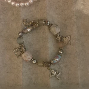 Charmigt armband med berlocker - Unikt armband med olika berlocker och pärlor i mjuka färger. Armbandet har detaljer som hjärtan, fjärilar och en ängel. Perfekt för att ge en personlig touch till din stil.