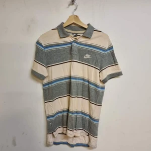 Randig pikétröja från Gant - Säljer en randig pikétröja från Gant i grått, beige och blått. Tröjan har korta ärmar och en klassisk krage. Perfekt för en avslappnad stil. Hör av dig vid intresse!