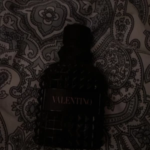Valentino born in roma  - Snygg parfymflaska från Valentino i en mörk, nästan svart färg. Flaskan har en unik design med nitar och ett elegant mönster. Perfekt för den som vill ha en stilren och lyxig doftupplevelse. 25 ml halv kvar!!!