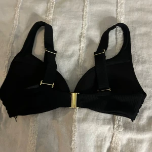 Svart bikiniöverdel från H&M - Snygg svart bikiniöverdel från H&M med justerbara axelband och gulddetaljer. Perfekt för en stilren look på stranden eller vid poolen. Enkel att matcha med olika underdelar.